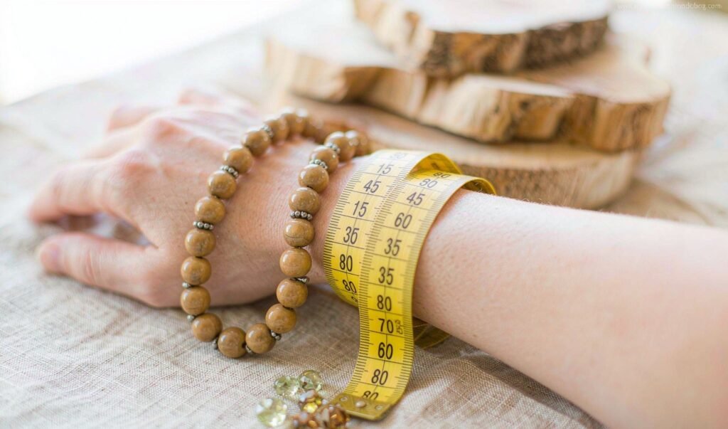 A tailor's measuring tape wrapped around a wrist beside wooden and gemstone bead bracelets